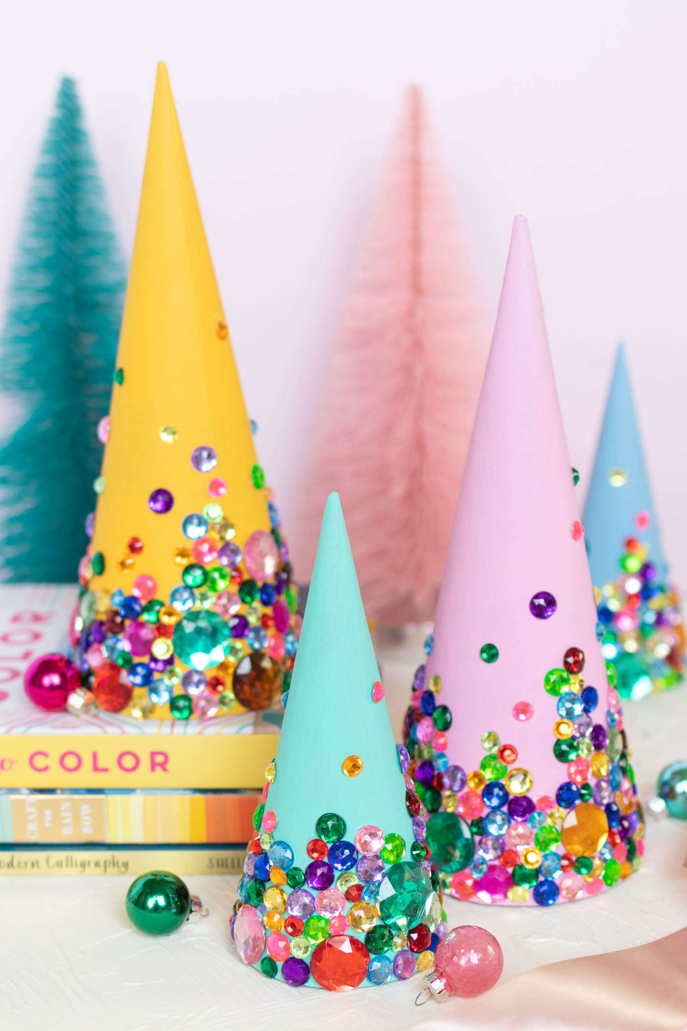 DIY Colorful Rhinestone Tree Decorations // Decorate mache cones with colorful paint and rhinestones to make sparkly tree decorations! These easy DIY Christmas trees make great mantel decor or shelf accessories for the holiday season! #christmasdiy #christmas #christmasdecor #painting #rhinestones #holidaydecor