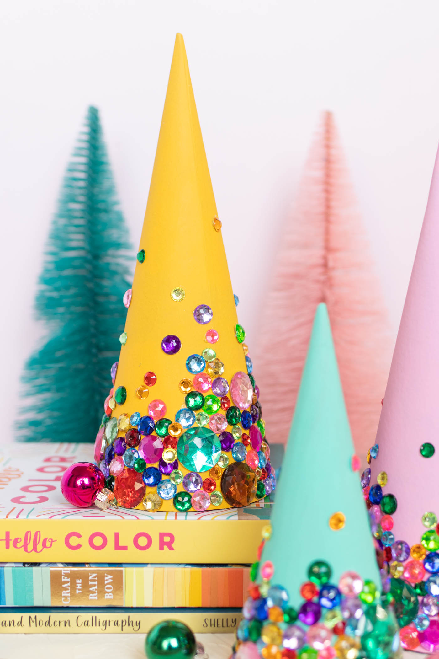 DIY Colorful Rhinestone Tree Decorations // Decorate mache cones with colorful paint and rhinestones to make sparkly tree decorations! These easy DIY Christmas trees make great mantel decor or shelf accessories for the holiday season! #christmasdiy #christmas #christmasdecor #painting #rhinestones #holidaydecor