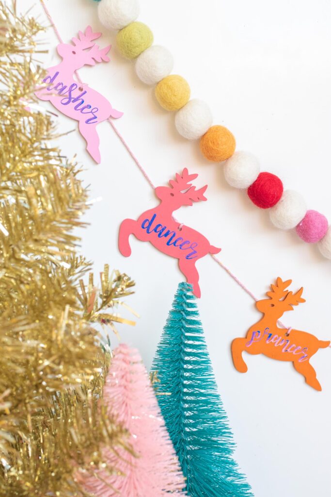 DIY Rainbow Reindeer Garland for Christmas // Paint wooden reindeer ornaments and add holographic vinyl to make a colorful Christmas garland with the names of Santa's reindeer! #christmasdecor #christmas #christmasdiy #rainbowdiy #reindeer #vinyl #cricut #painting