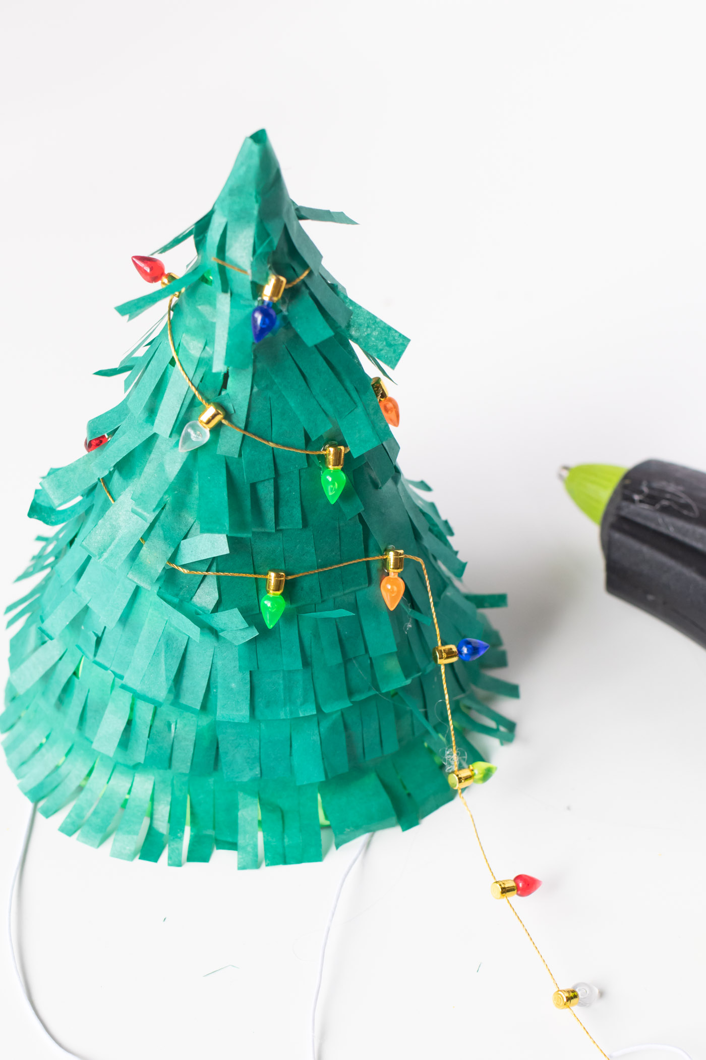 DIY Christmas Tree Party Hats // Turn a plain party hat into a fun holiday craft with tissue paper! Upcycle your hats into fringed Christmas trees decorated with lights and ornaments! #christmas #christmasdiy #christmascrafts #partydiy #partyideas #holidayparty #christmasparty #partyhats