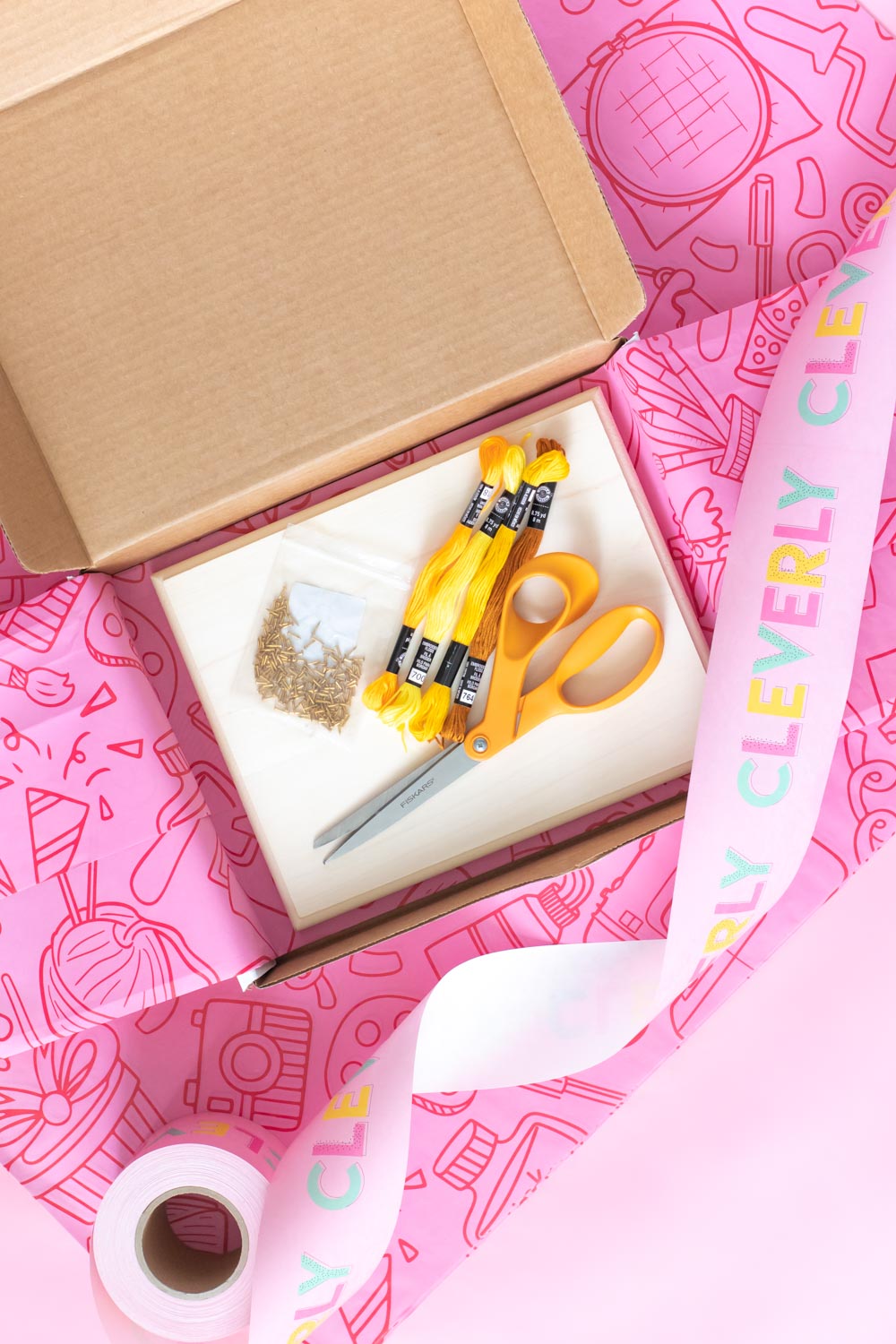 shipping box with craft supplies on pink background