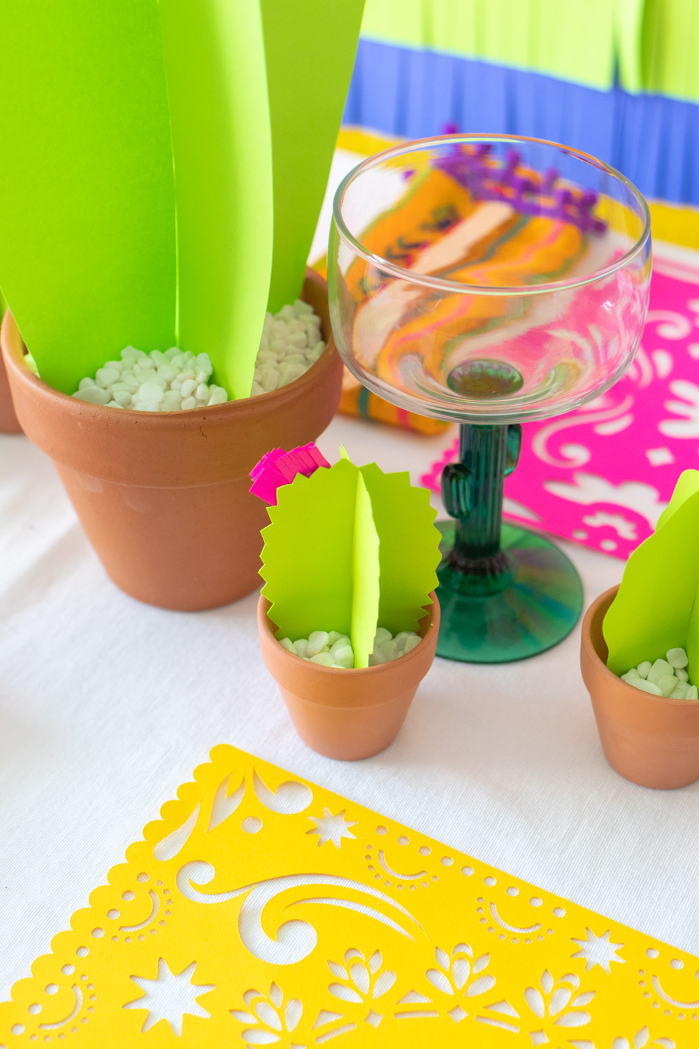 mini paper cacti in pots on tablecloth with glassware and paper placemats 