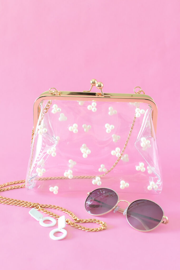 clear pearl stadium bag next to sunglasses and earrings