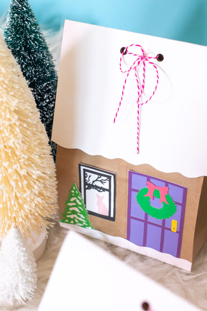 paper pieces decorate gingerbread house paper gift bags surrounded by trees