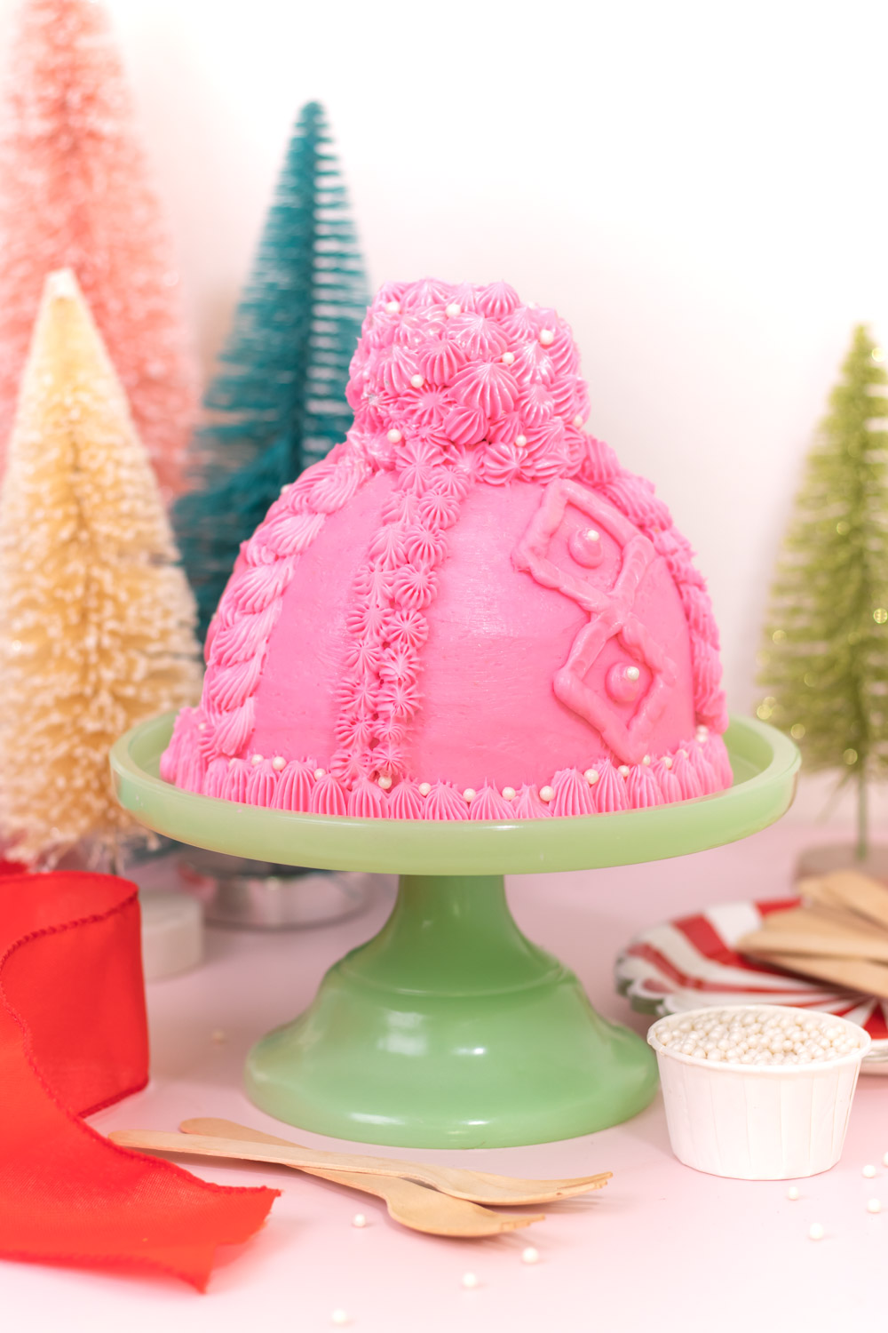 knit beanie cake on cake stand in front of christmas trees