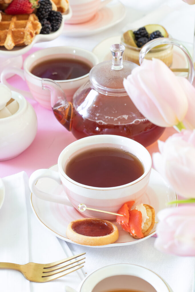 teacup with treats on pink and white tablecloth at spring tea party